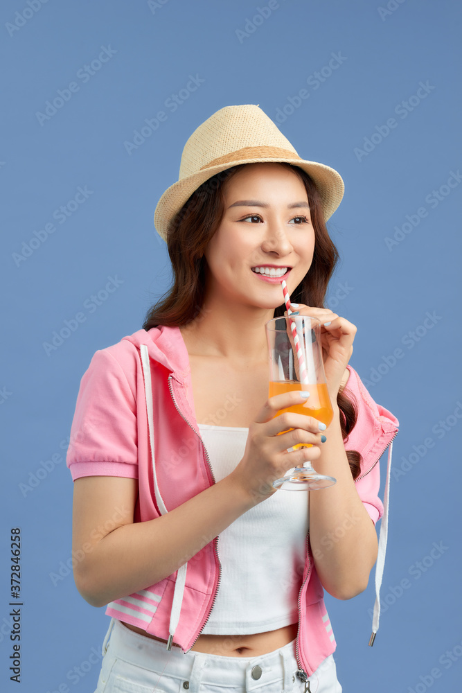 迷人的年轻亚洲女性在蓝色背景下喝果汁。