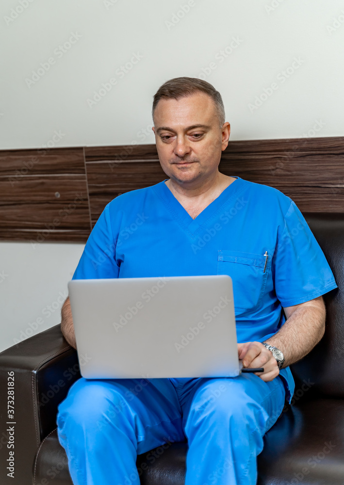 塞尔维亚男医生在笔记本电脑上阅读医疗结果。坐在沙发上。现代医院办公室背景