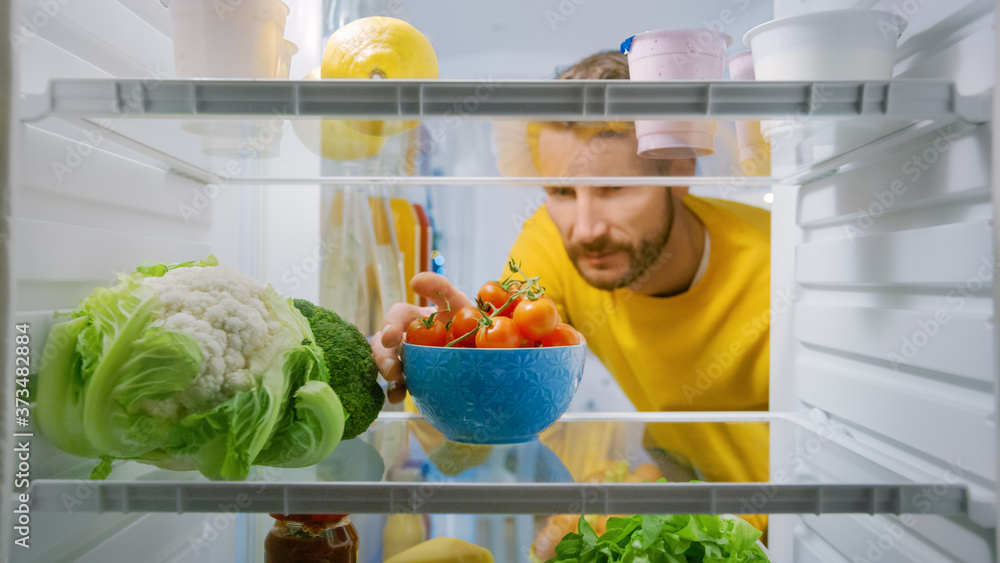 厨房冰箱里：英俊男子从打开的冰箱里拿走樱桃番茄。男子准备健康