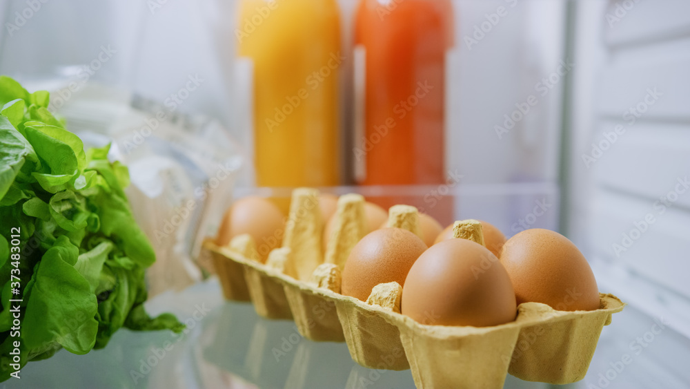 Shot from Inside the Kitchen Fridge: Box Pack of Eggs, Fresh Juices and Green Vegetables. Point of V