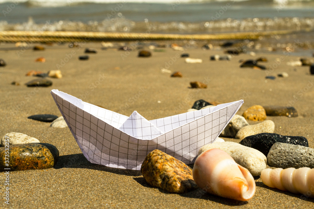 在海浪的背景下，沙滩上的纸船在贝壳和石头之间。复制空间。