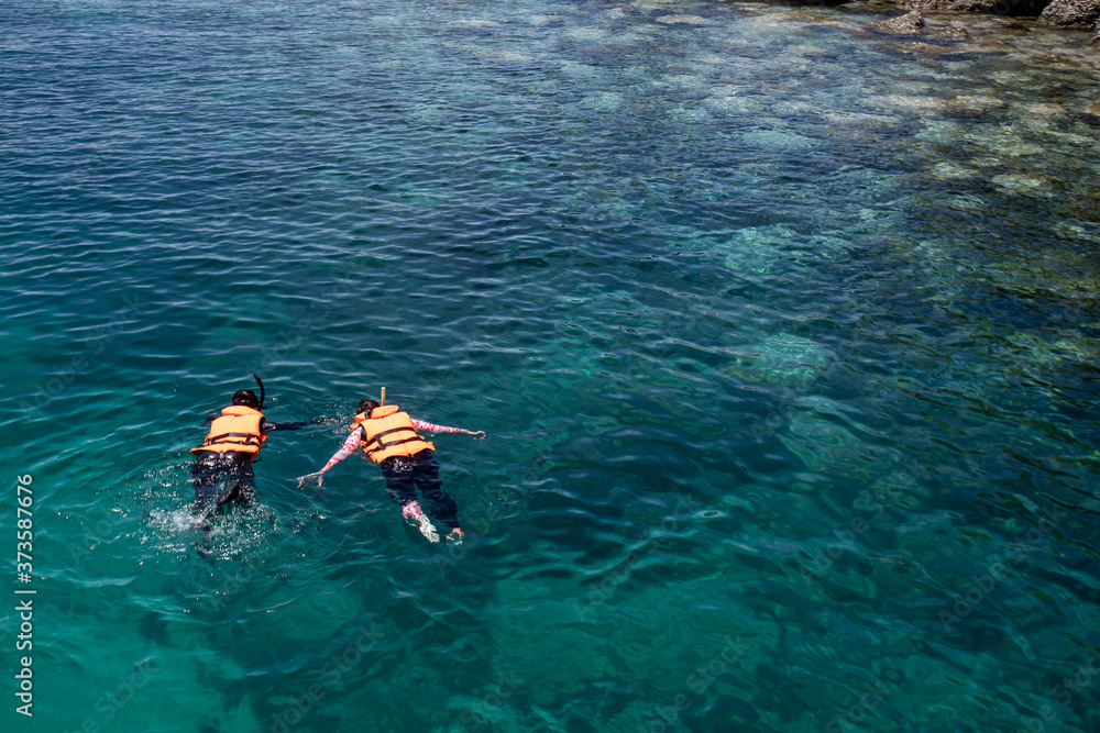 两人穿着救生衣在热带海水清澈的珊瑚礁上浮潜