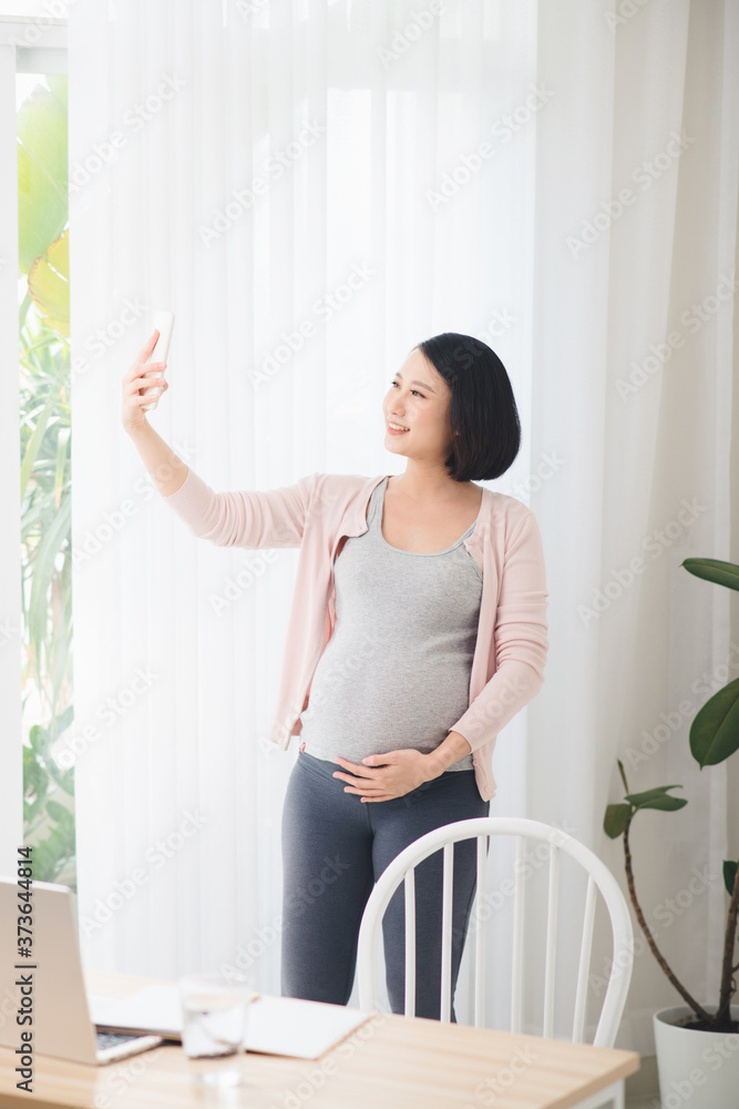 怀孕的博主在手机上自拍。怀孕的自由职业者在办公室拿着手机。