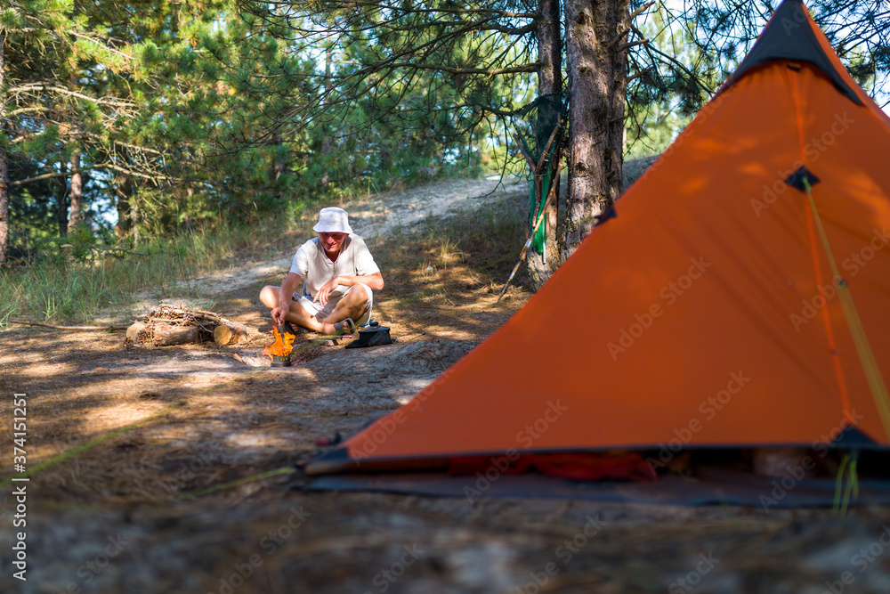 一名男子在松林中看着帐篷附近的篝火