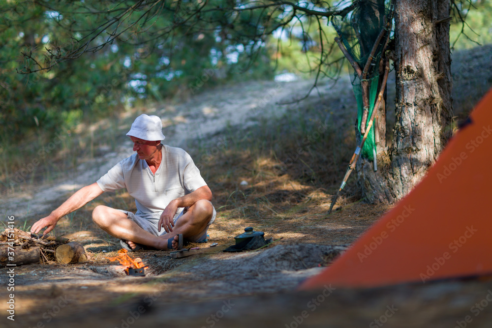 一名男子在松林中看着帐篷附近的篝火