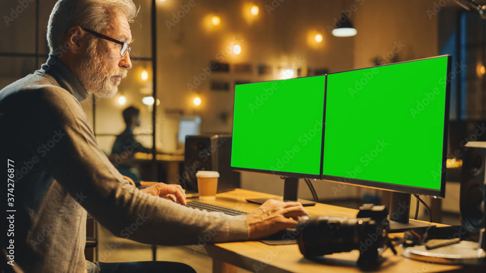 富有创意的中年设计师坐在桌子旁，用台式电脑配两个绿色模型尖叫