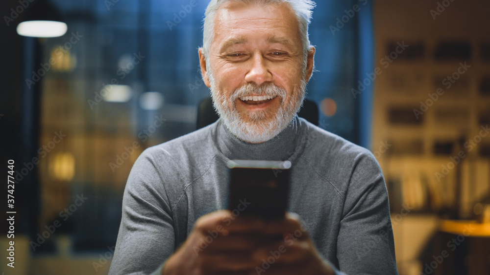 英俊成功的中年大胡子商人使用智能手机大笑的肖像