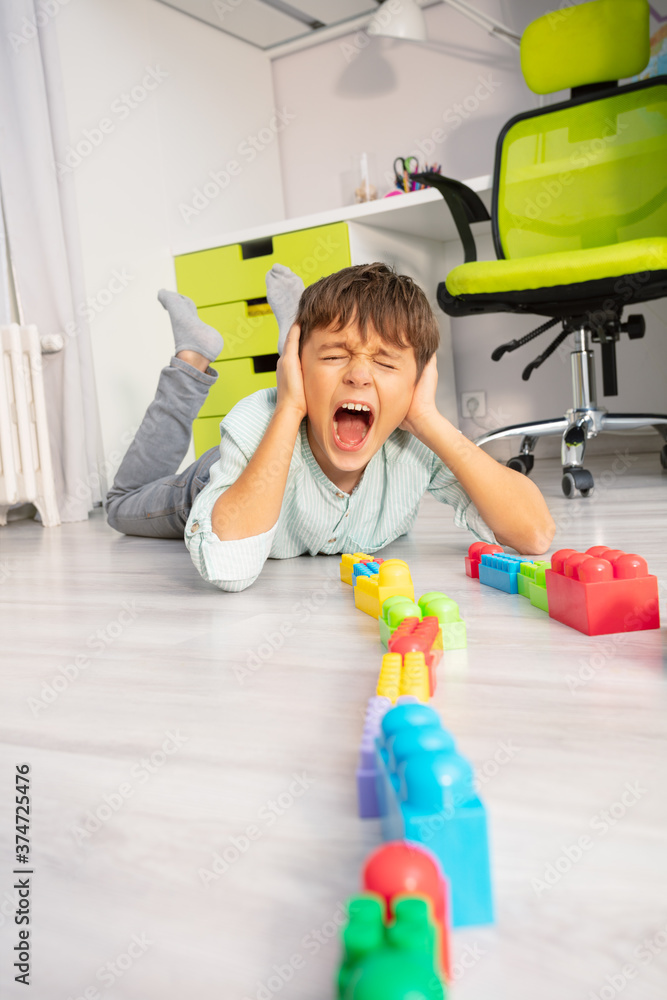 自闭症男孩把玩具排成一排躺在地板上尖叫并用手捂住耳朵