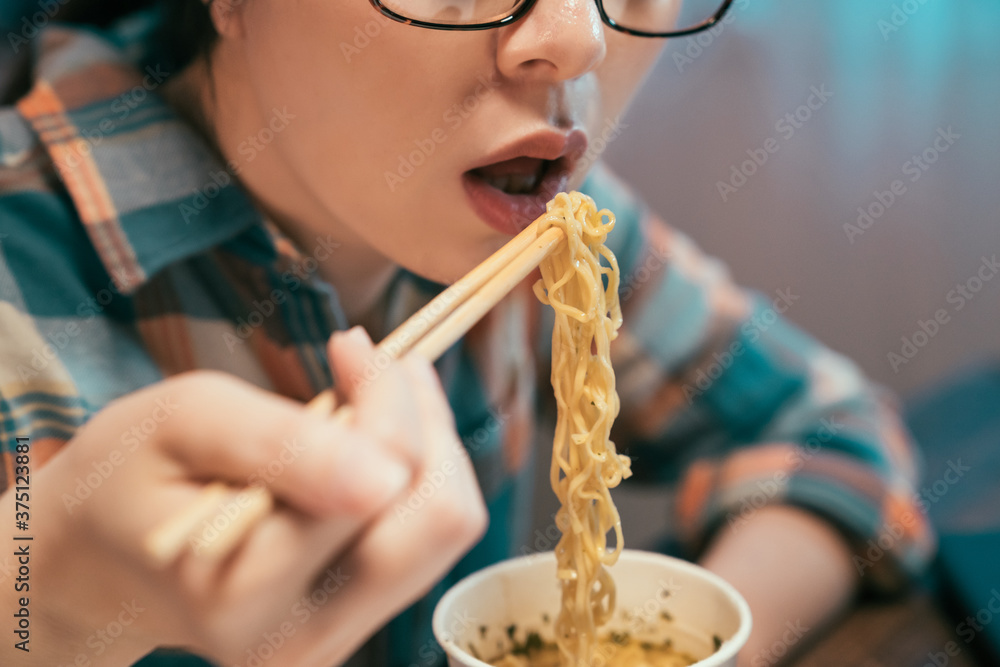 亚裔日本女性用筷子吃方便面。戴眼镜的女性近距离享受深夜