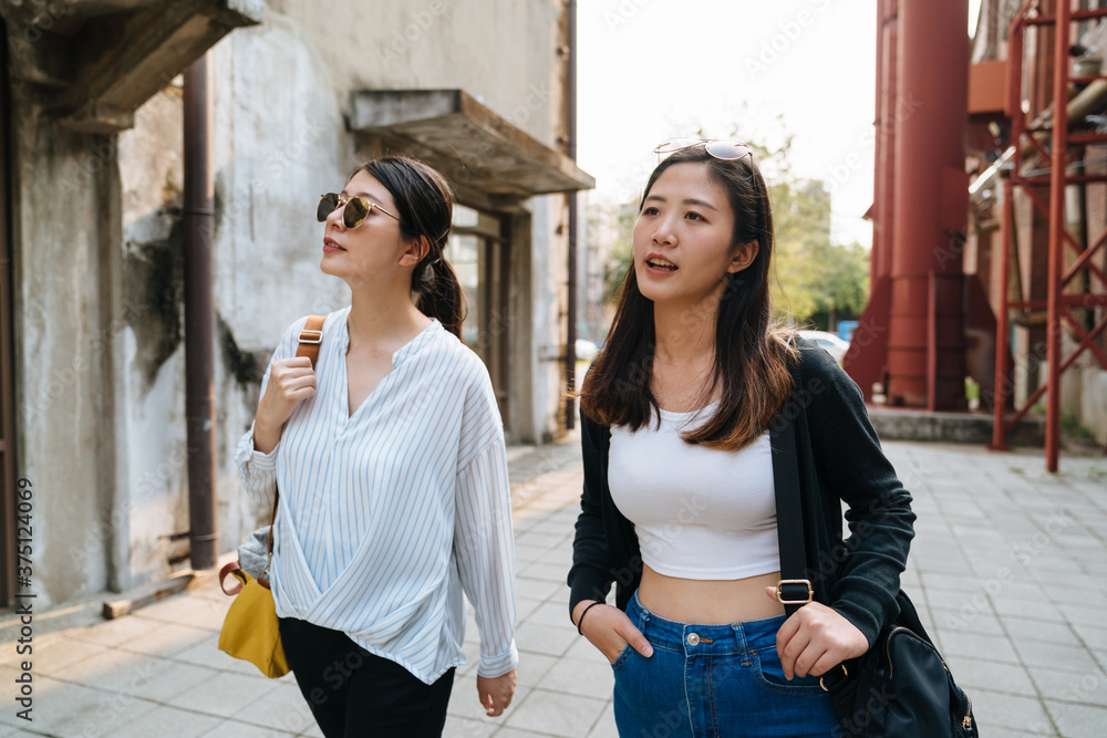 两个美丽的女孩在夏天的户外散步，参观古老的红色工厂。女性穿着时尚的短上衣