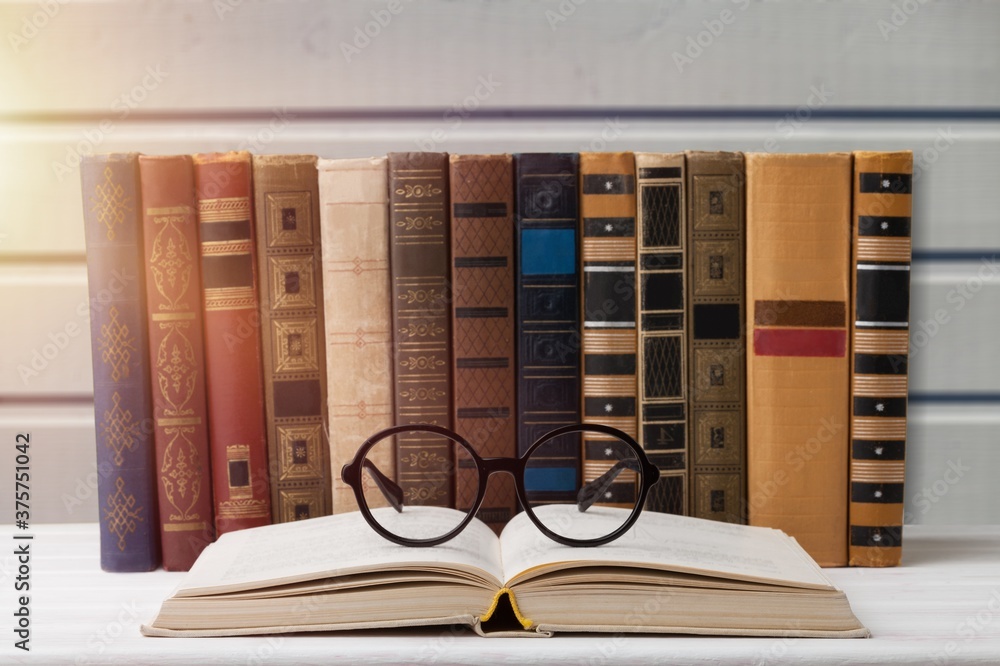 A stack of books with glasses for reading on the desk