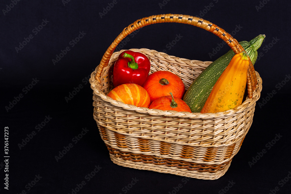 黑色背景柳条篮中五颜六色的有机蔬菜。南瓜、南瓜、西葫芦、胡椒。