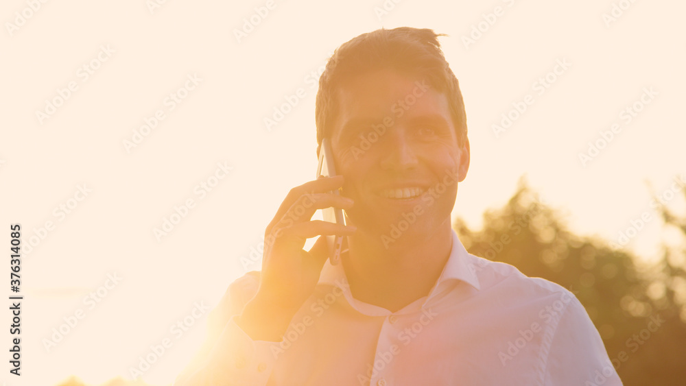 特写：成功的商人在金色的夏日日落时通过电话交谈。