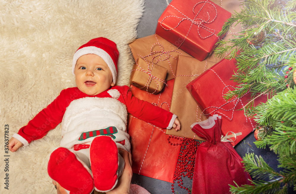 可爱的小男婴躺在地板上，放在一堆礼物盒子里，微笑着抬头看新年。