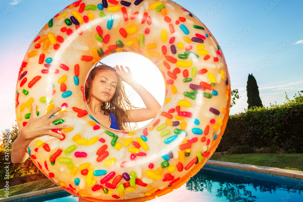 可爱冷静的少女站在游泳池附近拿着充气浮标甜甜圈肖像