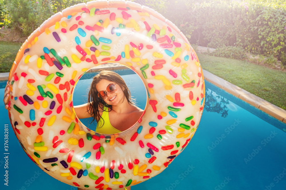 快乐微笑的少女站在游泳池边上，手里拿着充气浮标甜甜圈