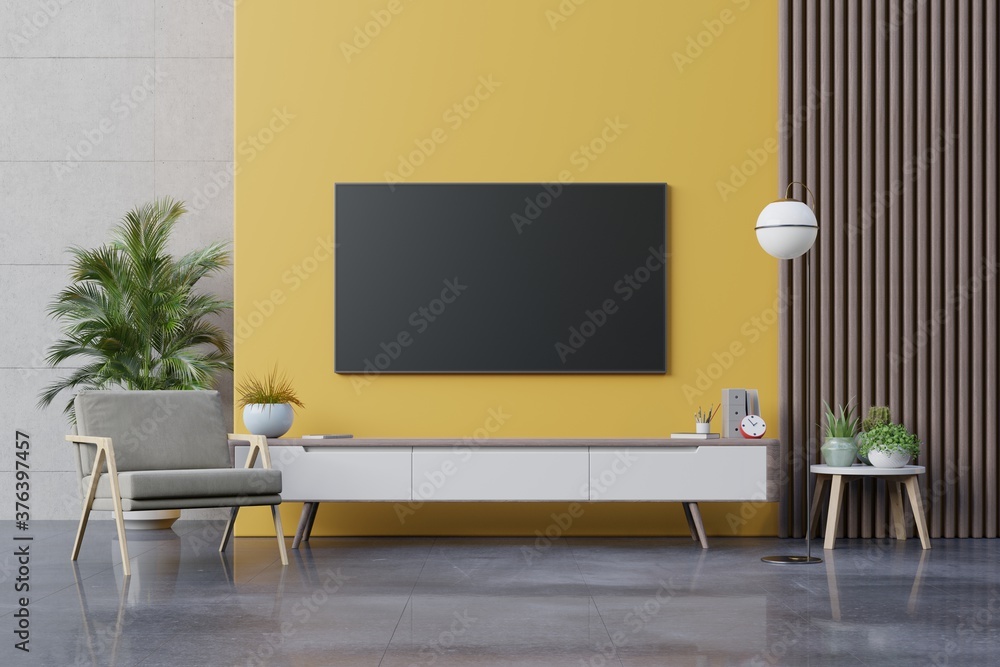 现代客厅橱柜上的电视，黄色墙壁靠背上有扶手椅、灯、桌子、花草