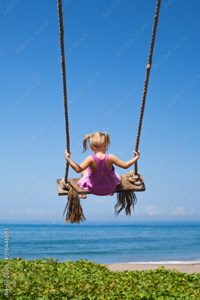 Happy girl have fun swinging high in mid air. Flying up upside down on rope swing on sea beach. Trav