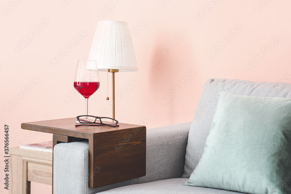 Glass of wine with eyeglasses on armrest table in room