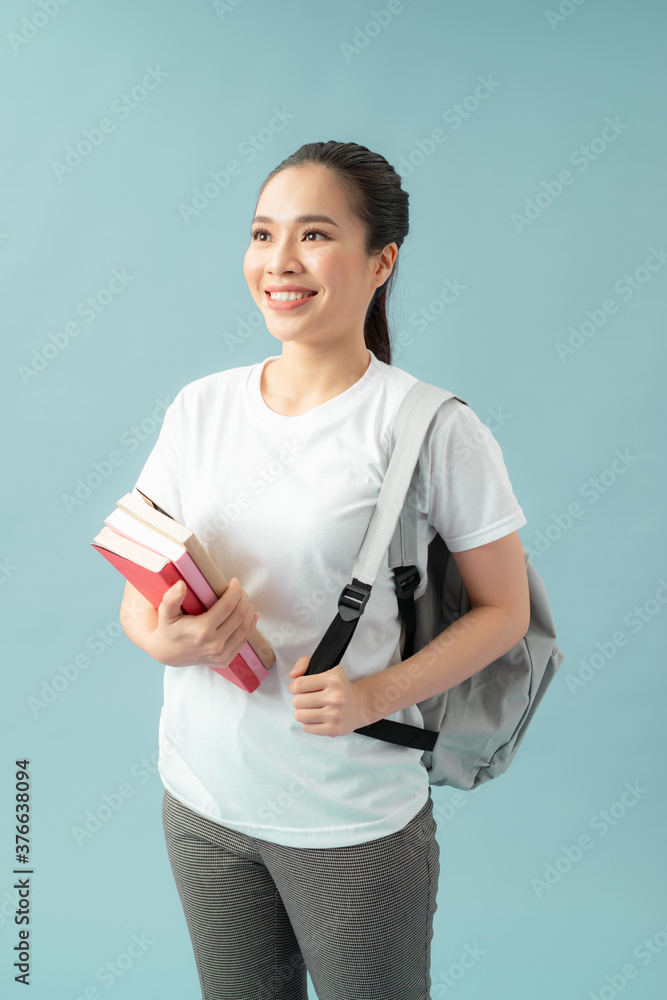 一个快乐友好的女学生的肖像，背着蓝色背景下孤立的书