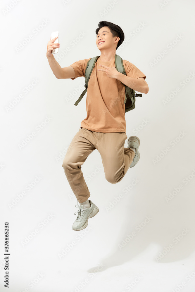 一个微笑的年轻人在白色背上独自跳跃时自拍的全长肖像