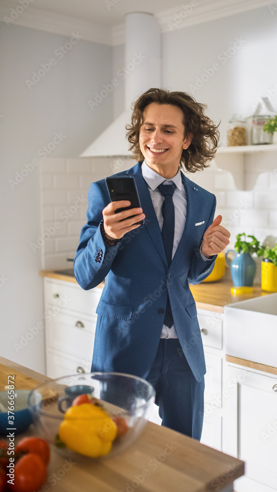 Happy Young Man with Long Hair Using Smartphone in a Kitchen while Wearing Blue Business Suit. He is