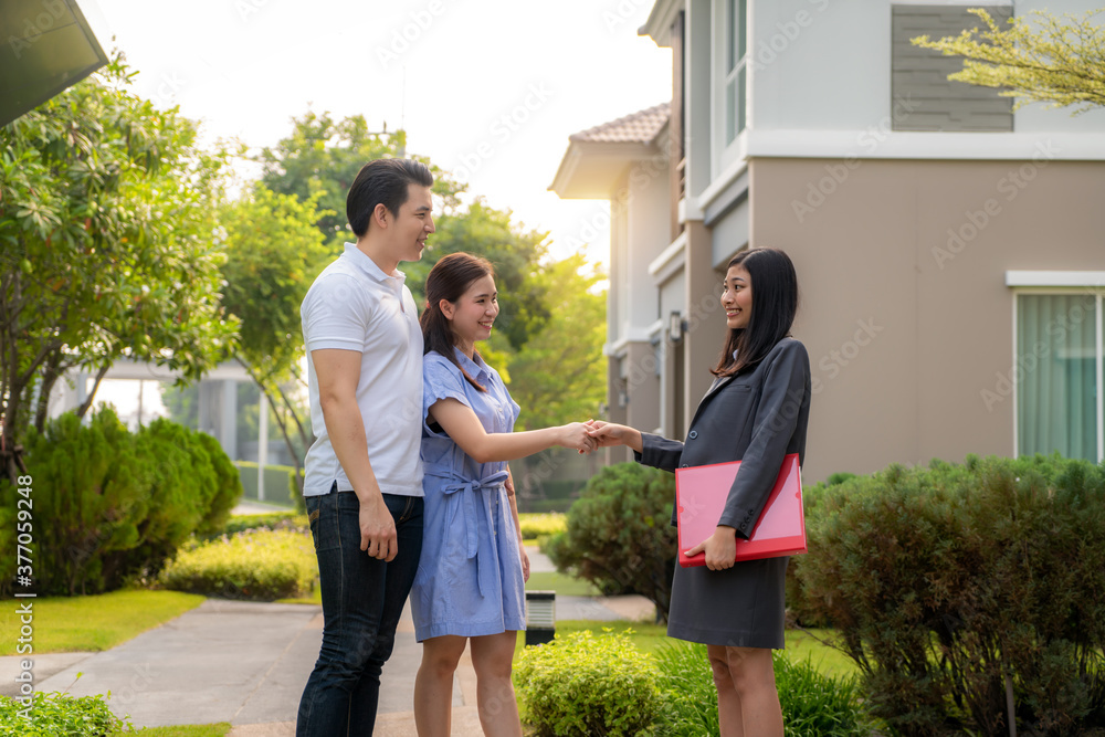 一对幸福的亚洲夫妇正在寻找他们的新房，并在交易后与房地产经纪人握手。