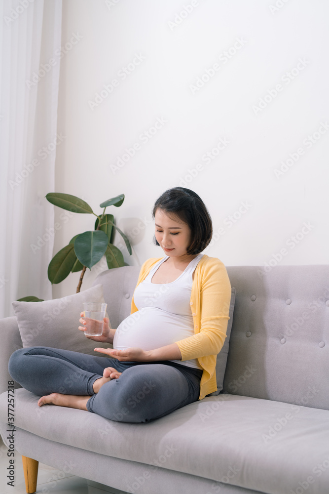 Portrait of young pregnant woman taking medicine and drinking water