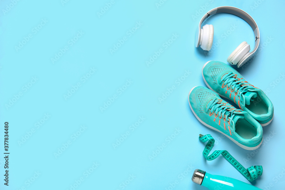 Sportive shoes, bottle of water, measuring tape and headphones on color background