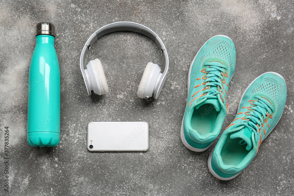 灰色背景的运动鞋、水瓶、手机和耳机