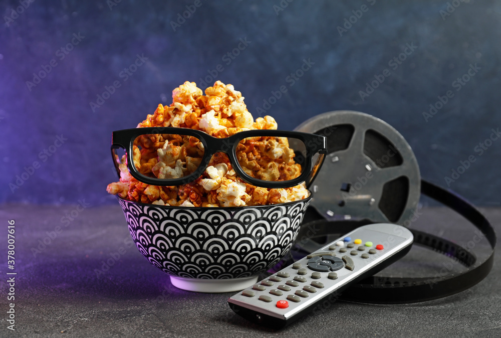 Popcorn, 3D glasses, remote control and film reel on dark background