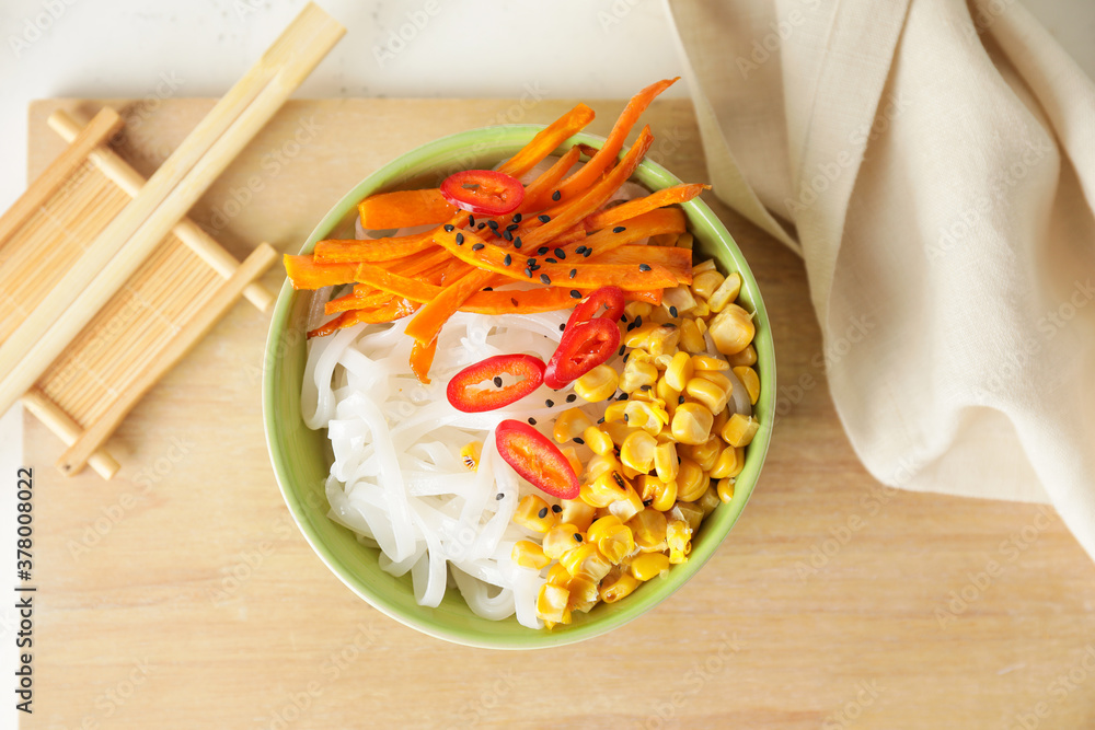Bowl with tasty rice noodles and vegetables on table