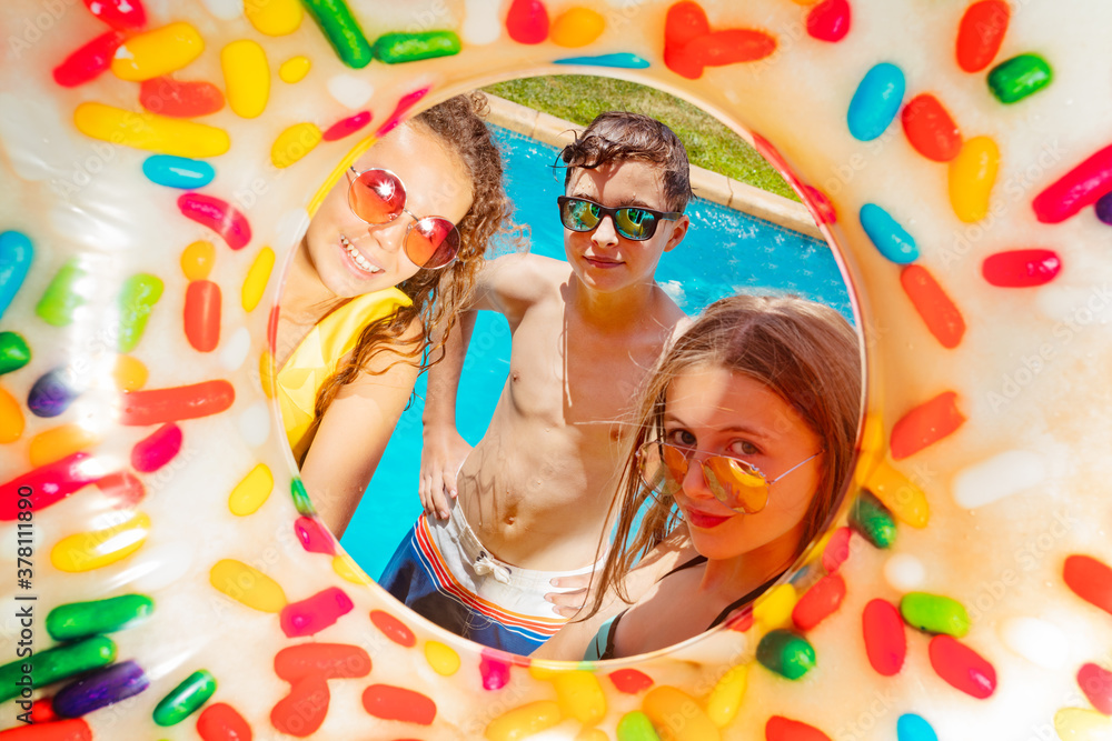 Three young kids inside the inflatable buoy smile wearing near swimming pool in sunglasses with nice