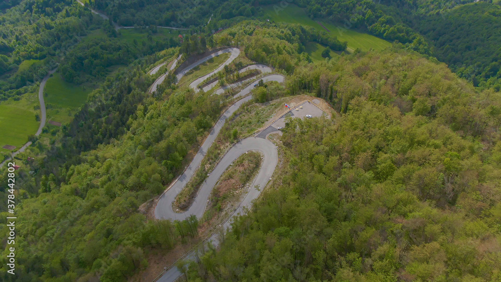 空中飞航：一条曲折的道路蜿蜒上一座森林覆盖的小山的电影镜头。