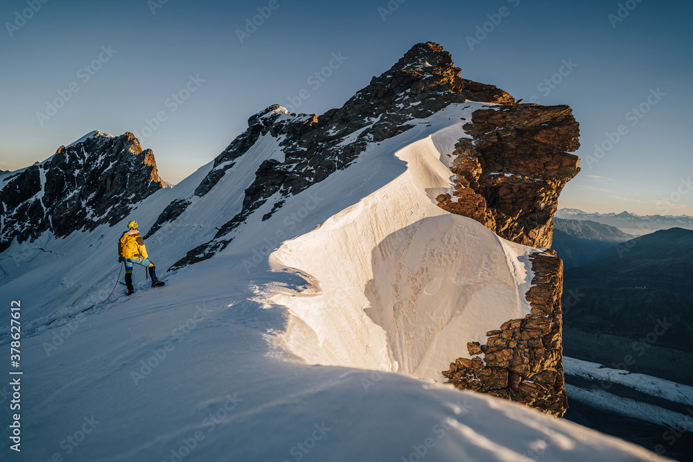 An alpinist climbing a rocky and snow mountain ridge during sunrise. Mountaineering and alpinism in 