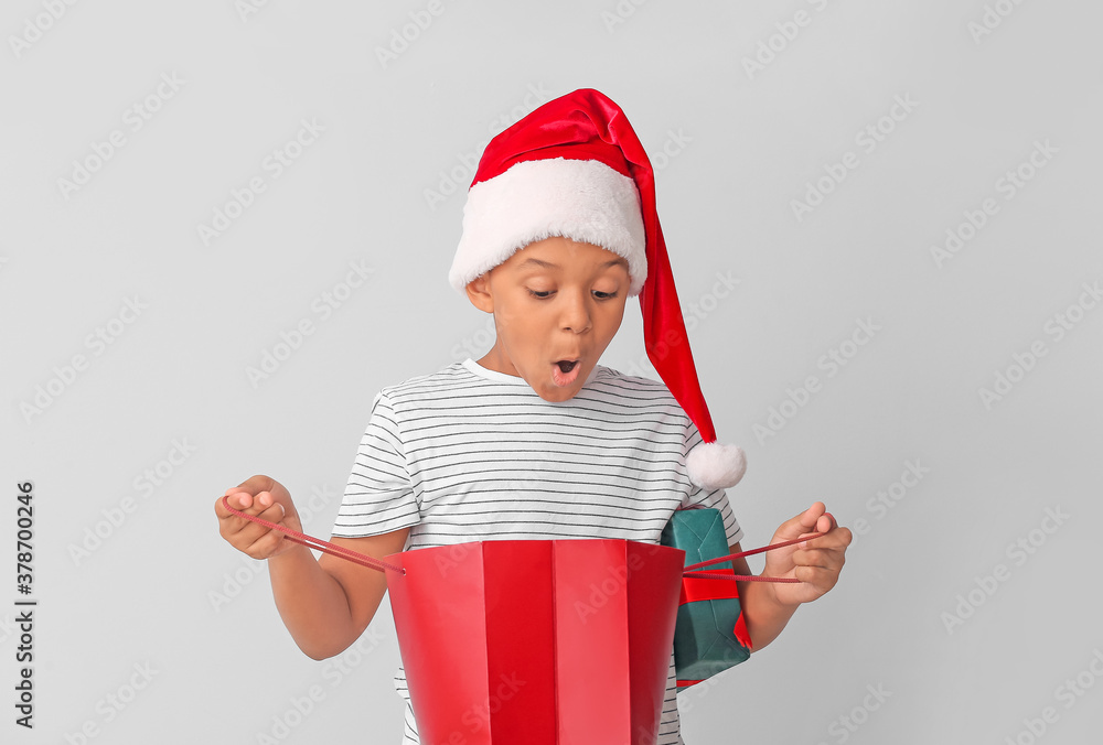 Cute African-American boy in Santa hat and with shopping bag on light background