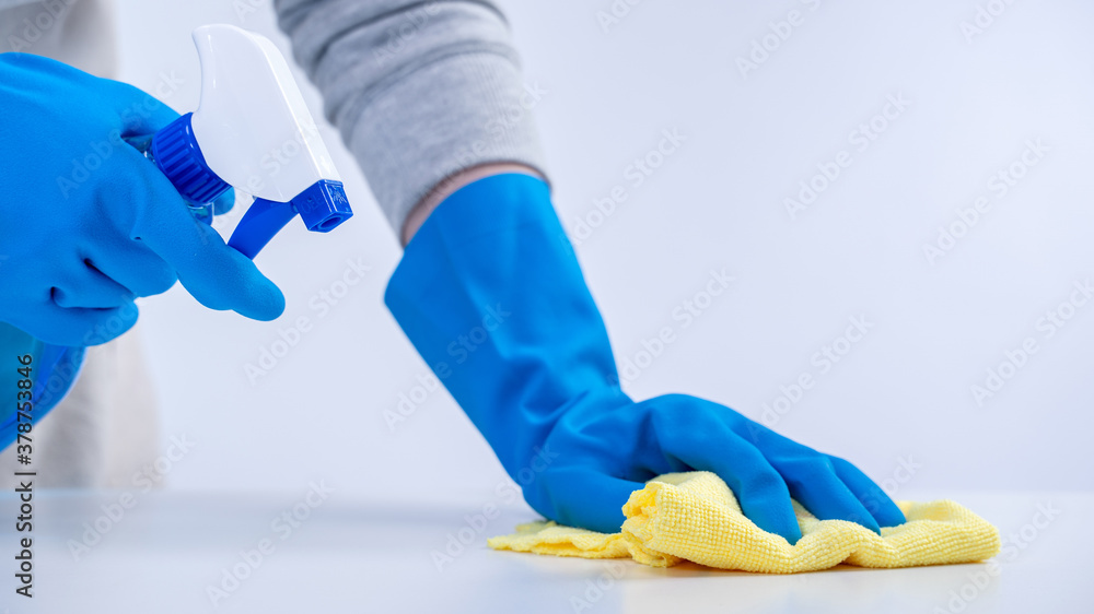Young woman housekeeper in apron is cleaning, wiping down table surface with blue gloves, wet yellow