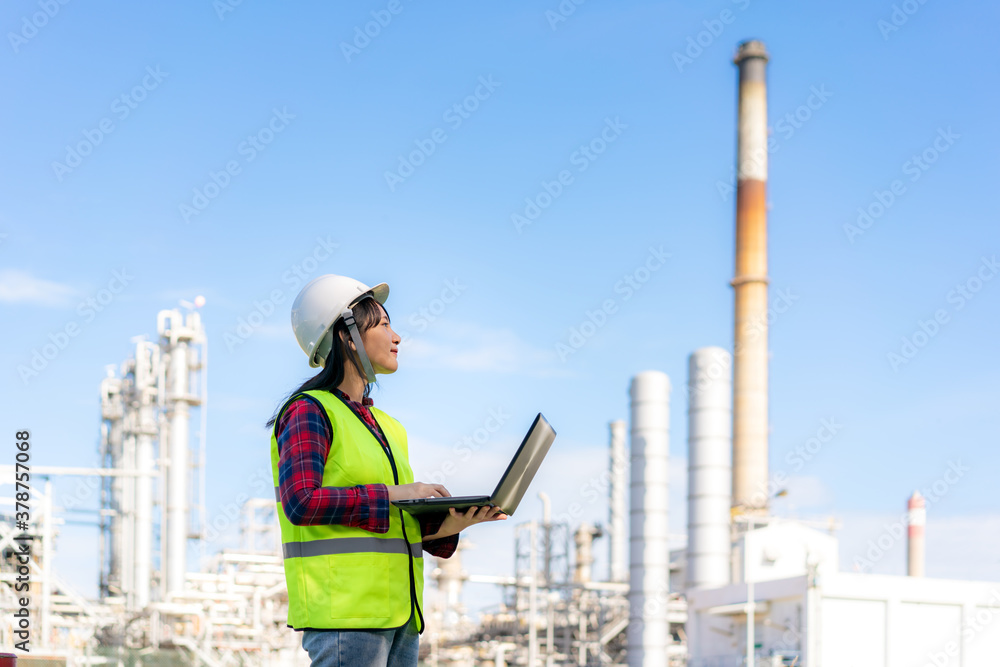 Asian woman petrochemical engineer working at night with laptop Inside oil and gas refinery plant in