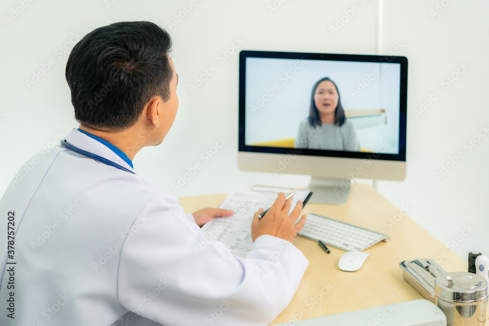亚洲男医生穿着白大褂，戴着耳机，在笔记本电脑上使用视频会议