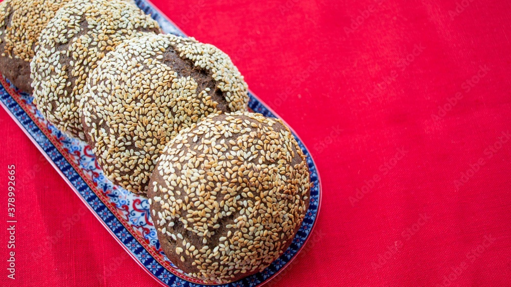 Composition in natural light. Homemade rye buns with sesame seeds on a colored plate, on a red flax 