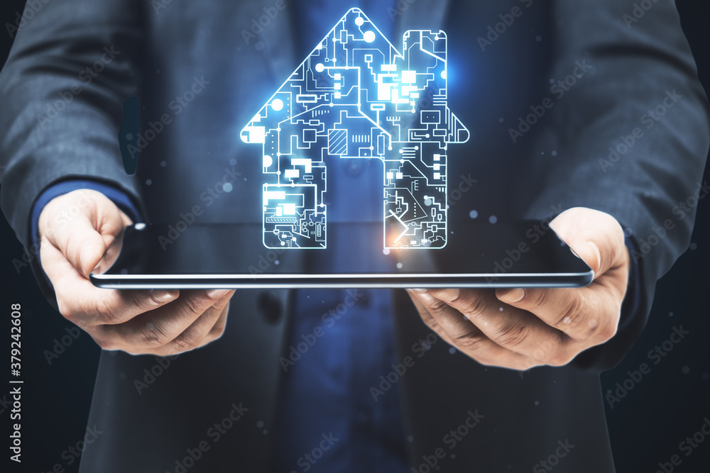 Businessman holding digital tablet with circuit house hologram.