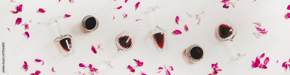 Red wine in glasses. Flat-lay of wine glasses with red wine and pink flowers petals over white backg
