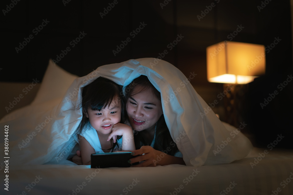 Asian happy family mother and little daughter watching movie or cartoon in smartphone together and b