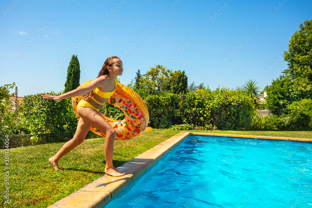 快乐的十几岁女孩，带着充气甜甜圈浮标，在游泳池里边跑边跳