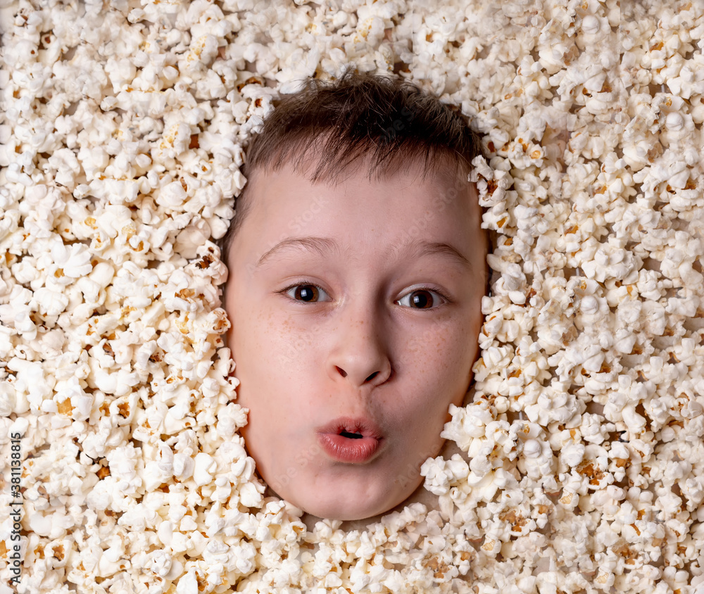 Cute happy pretty little boy`s face in popcorn. Top view on the child. Art photo.