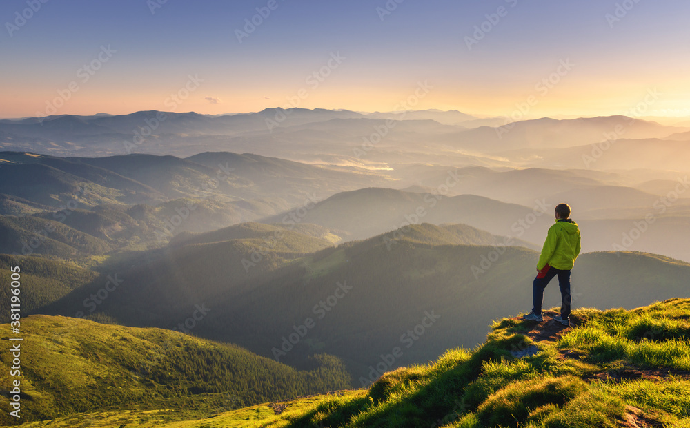 Sporty man on the mountain peak looking on mountain valley with sunbeams at colorful sunset in autum