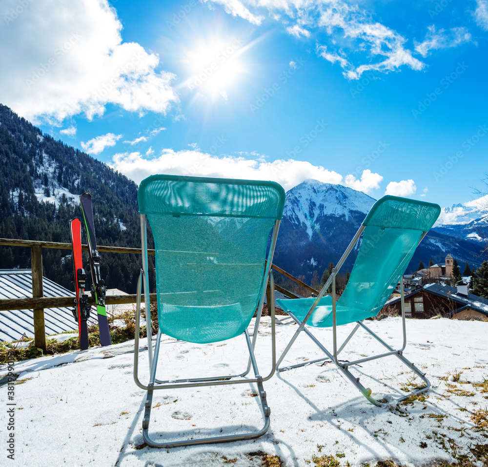 Pair of deck chairs near ski with mountains and Alpine peaks panorama on background