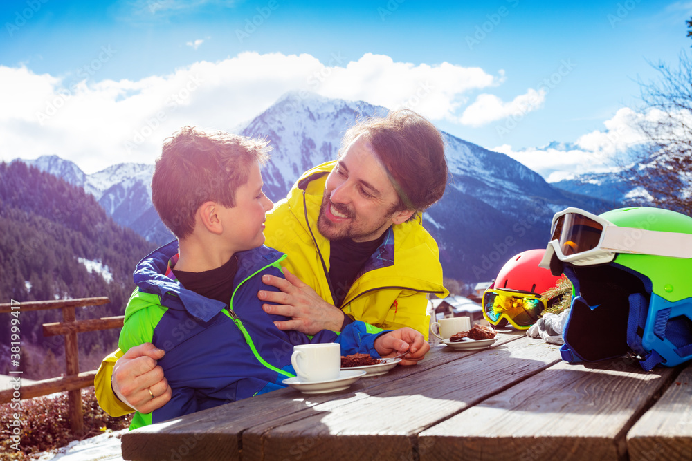 Father in ski outfit hug and look smiling to face little boy enjoy lunch break over mountain view af
