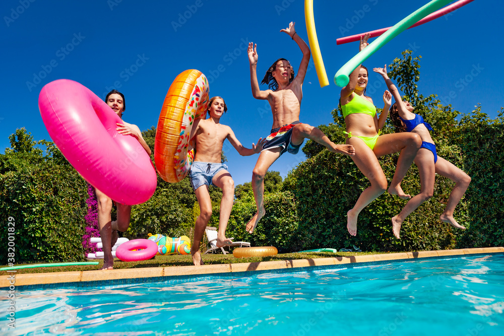 Group of teenage children have fun in the swimming pool diving with inflatable toys doughnuts jump a