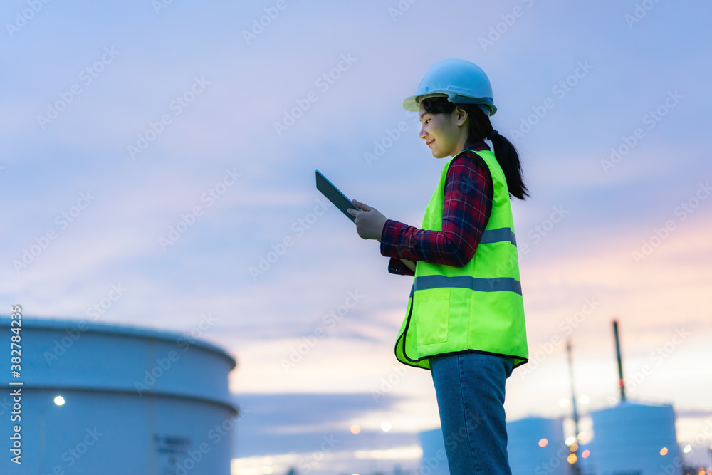 亚洲女性石化工程师在石油和天然气炼油厂内使用数字平板电脑夜间工作